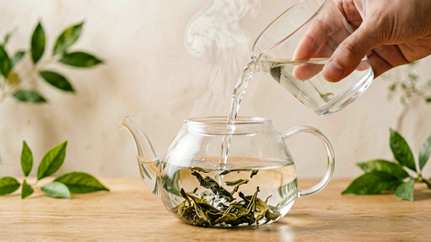 Hot water being poured into a glass teapot as loose tea leaves unfurl